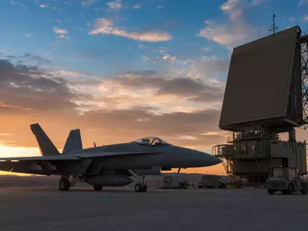 Northrop Grumman US6668071029 zeigt generischen Militärjet neben Radaranlage bei Sonnenuntergang auf Wüstenflugplatz - Foto: THN