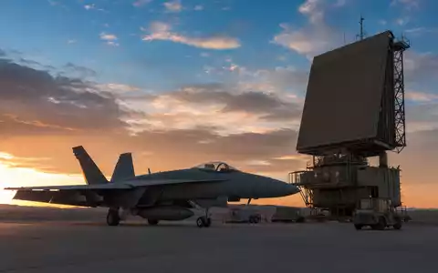 Northrop Grumman US6668071029 zeigt generischen Militärjet neben Radaranlage bei Sonnenuntergang auf Wüstenflugplatz - Foto: THN