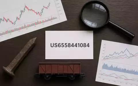 Norfolk Southern Corp. (US6558441084): Flatlay mit ISIN-Karte, rostigem Schienenspike und Miniatur-Güterwaggon auf Holztisch - Foto: THN