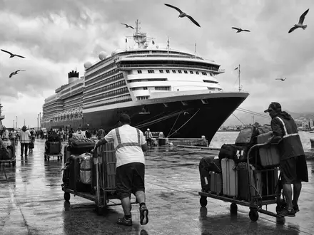 Norwegian Cruise Line BMG667211046 illustriert eine schwarz-weiße Hafenszene mit unbrandetem Schiff und rollenden Gepäckwagen - Foto: THN