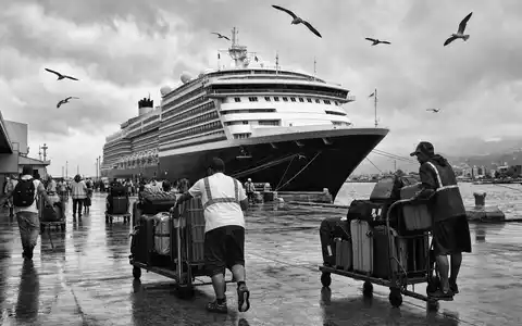 Norwegian Cruise Line BMG667211046 illustriert eine schwarz-weiße Hafenszene mit unbrandetem Schiff und rollenden Gepäckwagen - Foto: THN