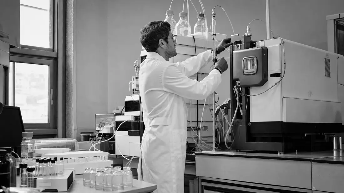 Schwarzweiß-Reportage: Techniker an chromatographischem Analysegerät im Labor