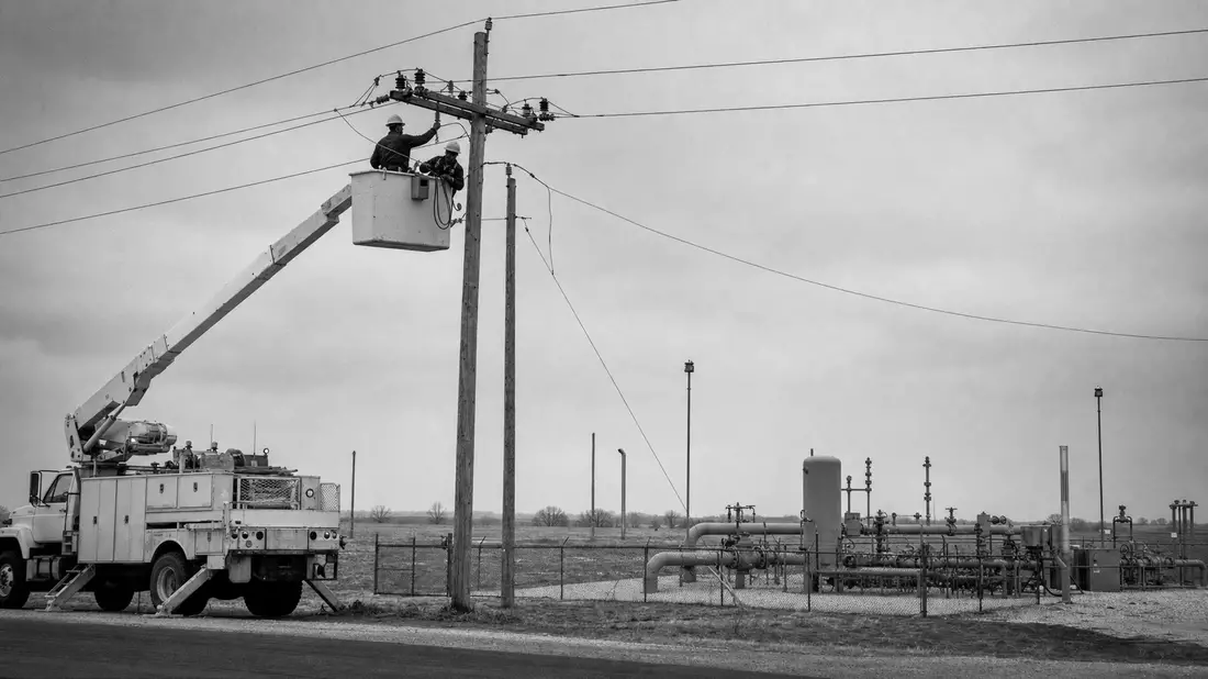 Schwarzweißfoto von Leitungsmonteuren am Strommast neben Erdgasstation