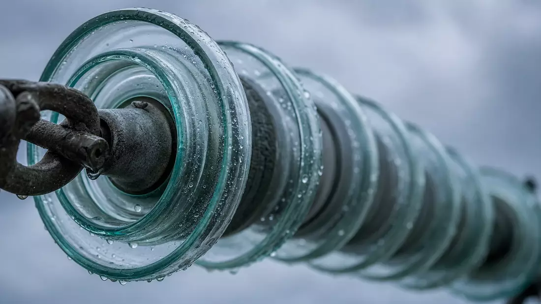 Makroaufnahme eines Glas-Isolators an Hochspannungsleitung mit Tropfen