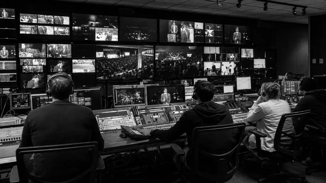 Schwarzweiß-Reportage im TV-Kontrollraum, Operatoren an Mischpulten vor Monitorwand