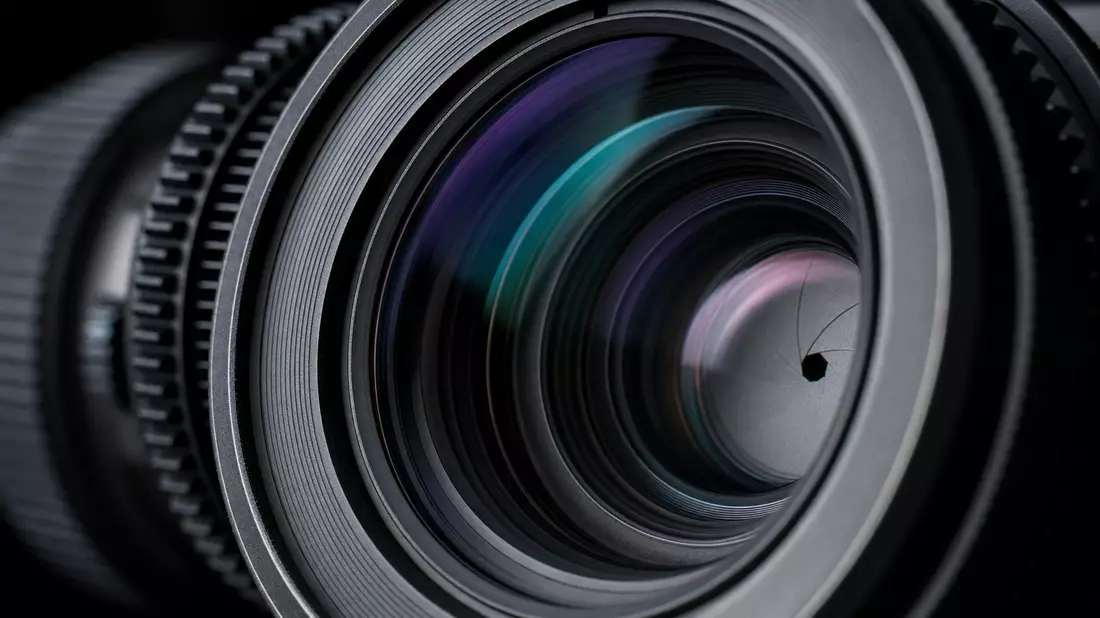 Makro-Detailaufnahme professionelles Kameraobjektiv Aperturblätter violette Lichtreflexion dunkler Hintergrund