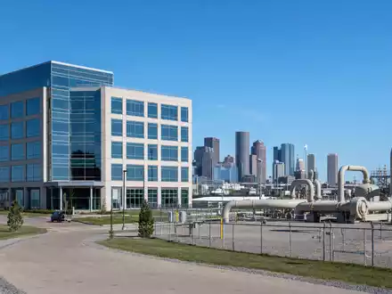 Loews Corporation US5404241031 zeigt fotorealistisch ein modernes Bürogebäude neben einer Erdgas-Pipelineanlage vor der Stadtskyline - Foto: THN