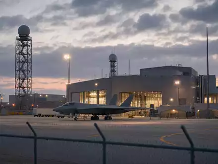 Fotorealistische Werksanlage von Lockheed Martin (ISIN US5398301094) mit Hangar und unmarkiertem Tarnkappenjet bei Dämmerung - Foto: THN
