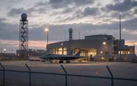 Fotorealistische Werksanlage von Lockheed Martin (ISIN US5398301094) mit Hangar und unmarkiertem Tarnkappenjet bei Dämmerung - Foto: THN
