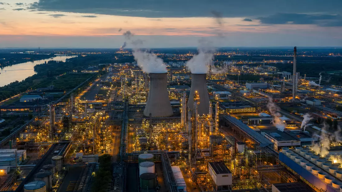 Fotorealistisches Luftbild eines Polymerchemiewerks bei Dämmerung mit beleuchteter Industrieanlage