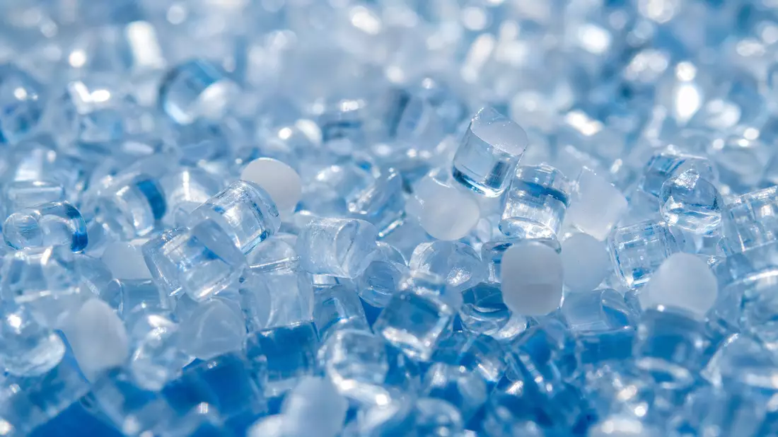 Extreme Makroaufnahme transparenter Polycarbonat-Granulatperlen mit Lichtbrechungsmustern und blauem Bokeh
