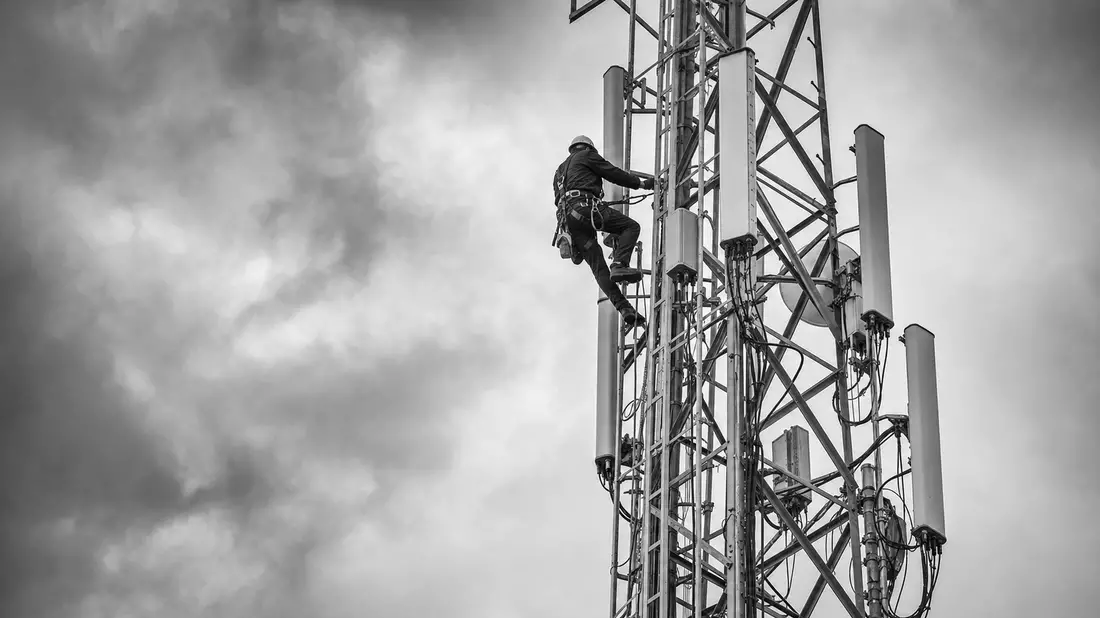 Schwarzweiß-Reportagefoto eines Turmmonteurs beim Aufstieg auf einen Mobilfunkmast