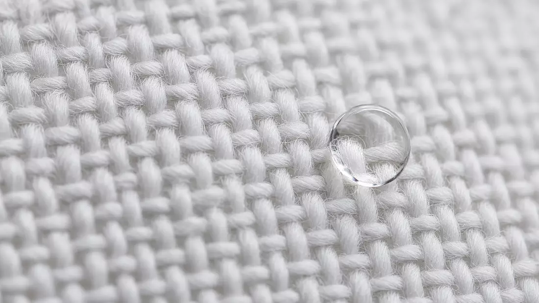 Makroaufnahme von weißem Textilgewebe mit Wassertropfen auf der Faserstruktur