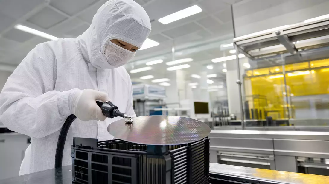Techniker im Reinraumanzug handhabt einen Silizium-Wafer in einer modernen Halbleiterfabrik