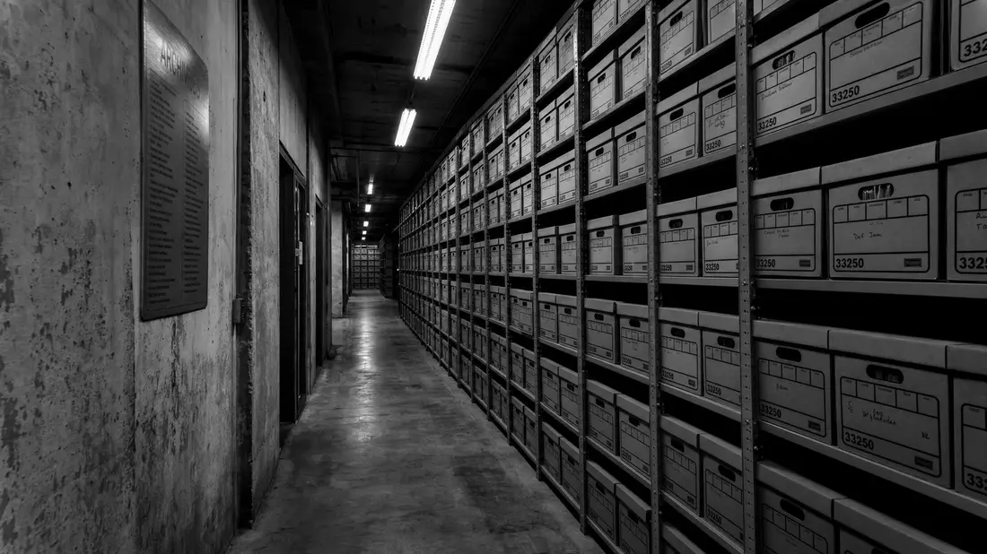 Schwarz-weiß Dokumentarfoto eines industriellen Archivkorridors mit Aktenkisten