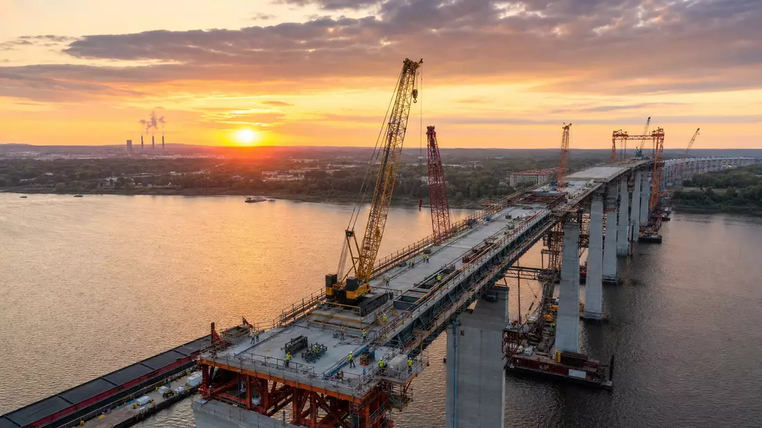 Fotorealistische Luftaufnahme einer Brückenbaustelle bei Sonnenuntergang mit Kränen und Stahlrahmen