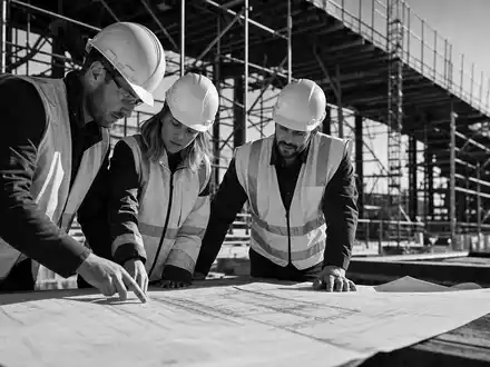 Jacobs Solutions Ingenieure prüfen Baupläne gemeinsam auf Großbaustelle in dokumentarischer Schwarzweißaufnahme, ISIN US4698141098 - Foto: THN