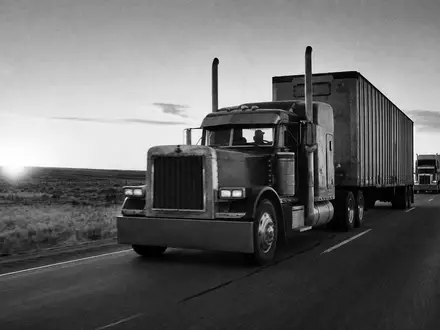 J.B. Hunt Transport US4655621062 – Dokumentarisches Schwarzweißfoto einer LKW-Kolonne auf amerikanischem Highway im Morgengrauen - Foto: THN