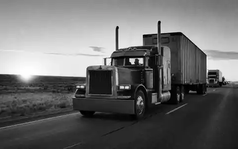 J.B. Hunt Transport US4655621062 – Dokumentarisches Schwarzweißfoto einer LKW-Kolonne auf amerikanischem Highway im Morgengrauen - Foto: THN