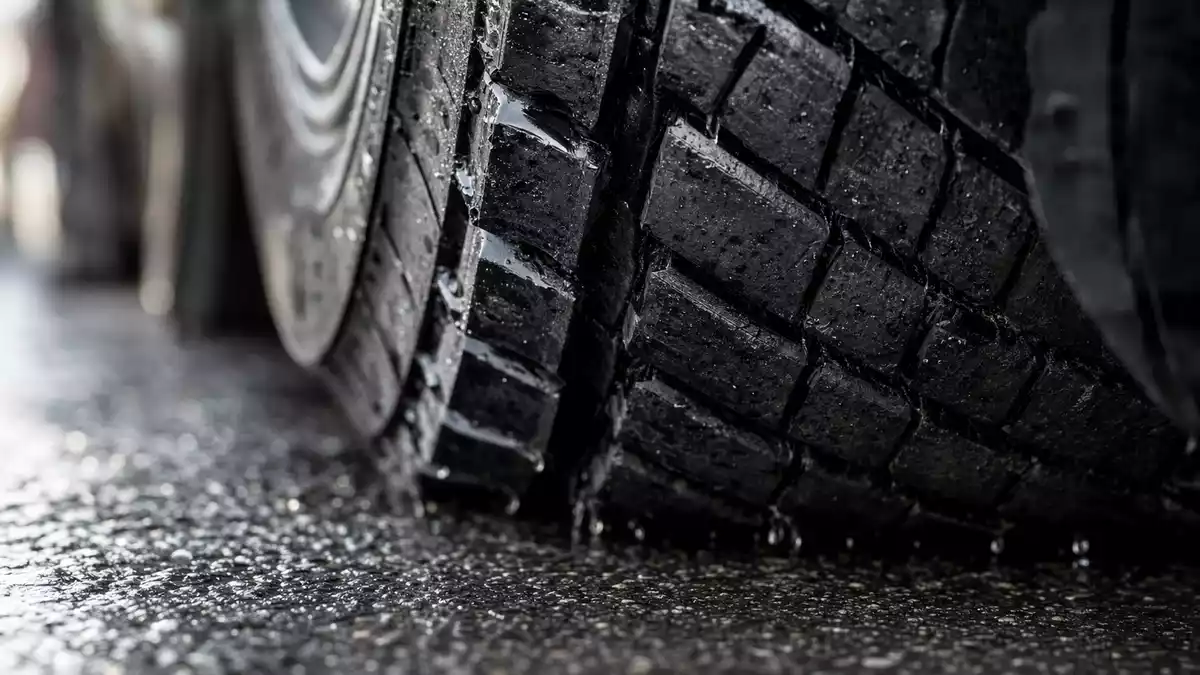 Extreme Makro-Nahaufnahme eines schweren LKW-Reifens mit nassen Profilrillen auf Asphalt