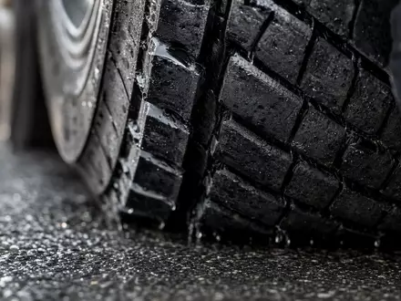 J.B. Hunt Transport US4655621062 – Makroaufnahme eines nassen LKW-Reifenprofils auf regennassem Asphalt mit Wassertropfen - Foto: THN