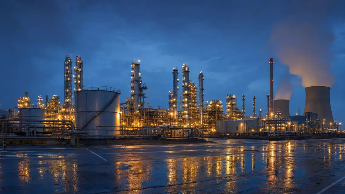 Beleuchtete Chemieanlage bei Nacht mit Dampf, Tanks und Rohrleitungen im Industriegebiet