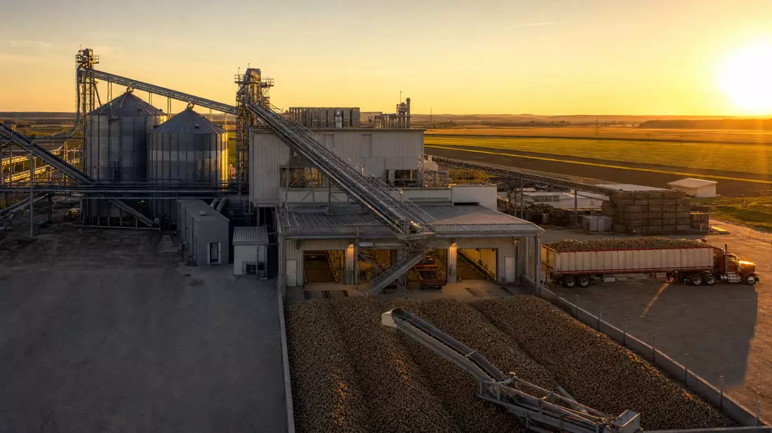 Industrielle Kartoffelverarbeitungsanlage bei Sonnenuntergang mit Silos und Lastwagen