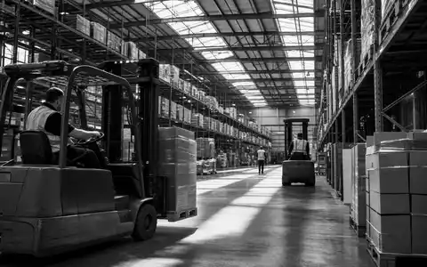 Schwarzweiß-Reportage dokumentiert Lagerhallenbetrieb von Tritax Big Box REIT plc, ISIN GB0008847096, mit Arbeitern und Gabelstaplern - Foto: THN