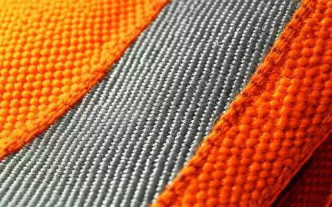 Serco Group plc GB0033055624 in Makroaufnahme, gewebte Warnschutz-Textilstruktur mit reflektierenden Streifen im Detail - Foto: THN