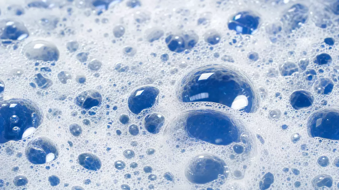 Makroaufnahme von Seifenschaum und blauen Wassertropfen mit glänzenden Reflexionen im Detail
