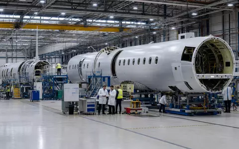 Dassault Aviation SA (FR0000121725): Industrielle Montagehalle zeigt Flugzeugrumpf-Sektionen, während Techniker sorgfältig die Bauteile prüfen - Foto: THN
