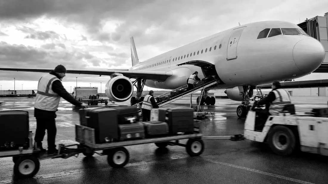 Schwarzweiß-Reportagefoto von Bodenpersonal bei Flugzeugabfertigung am Gate