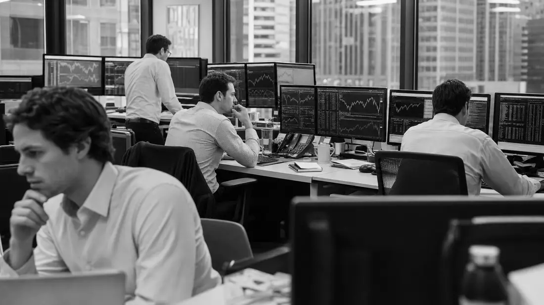 Schwarzweiß-Reportagefoto von Finanzanalysten an Multi-Monitor-Arbeitsplätzen