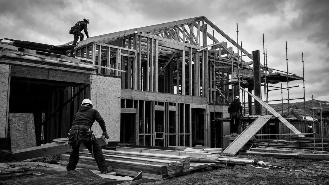 Schwarz-weiß Reportagefoto einer Baustelle mit Holzrahmenhaus und Arbeitern