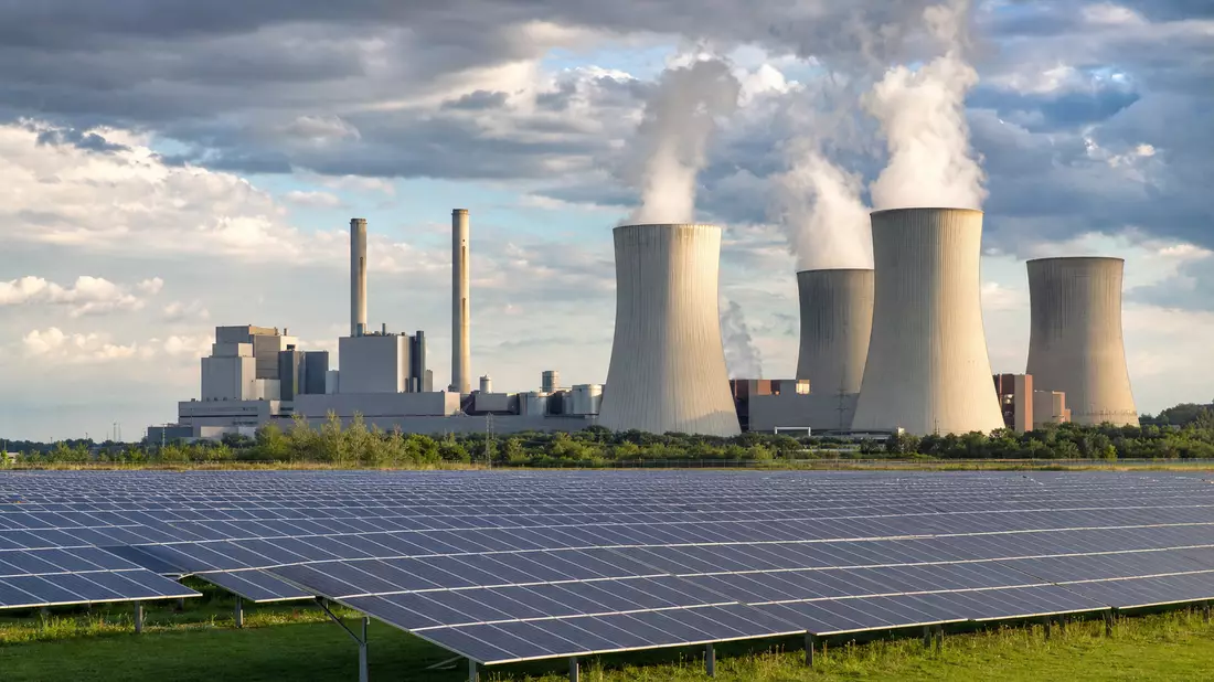 Generisches Kraftwerk mit Kühltürmen und Solar-Farm im Vordergrund unter bewölktem Himmel