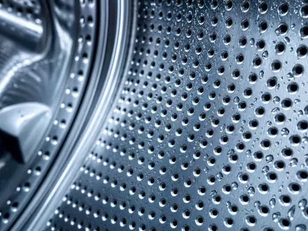 Whirlpool Corp. (US9633201069) fertigt Metallkomponenten, gezeigt in einer Makroaufnahme einer gelochten Edelstahltrommel mit Wassertropfen - Foto: THN