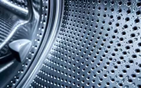 Whirlpool Corp. (US9633201069) fertigt Metallkomponenten, gezeigt in einer Makroaufnahme einer gelochten Edelstahltrommel mit Wassertropfen - Foto: THN