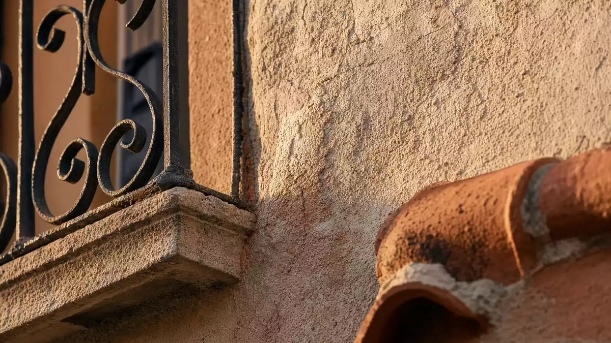Makroaufnahme einer Fassade mit schmiedeeisernem Balkongitter und Terrakotta-Dachziegel im Sonnenlicht