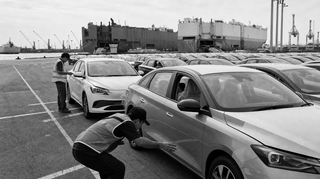 Schwarzweiß-Reportagefoto von Arbeitern bei Fahrzeugkontrolle auf Logistikhof am Hafen