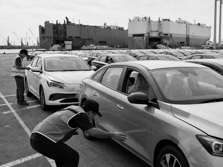 Inchcape plc GB00B61TVQ02 dokumentiert eine Schwarzweiß-Reportage-Aufnahme von Arbeitern bei sorgfältiger Fahrzeugkontrolle direkt am Hafen - Foto: THN