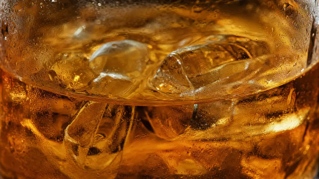 Makroaufnahme von bernsteinfarbenem Getränk mit Eiswürfeln und Kondenswasser im Glas