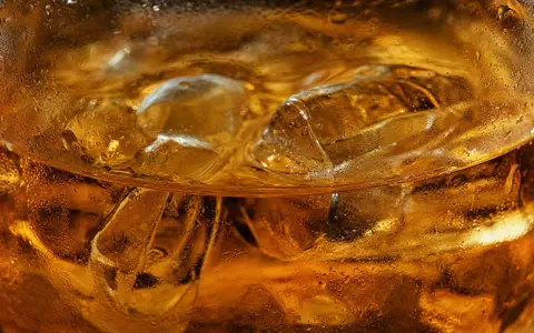 Diageo plc GB0002374006 zeigt eine Makroaufnahme bernsteinfarbener Spirituose mit Eiswürfeln und feinen Kondenswassertropfen im Glas - Foto: THN