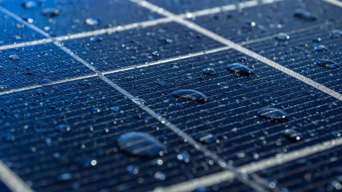 Makroaufnahme einer blauen Solarzellenoberfläche mit feinen Leiterbahnen und Wassertropfen
