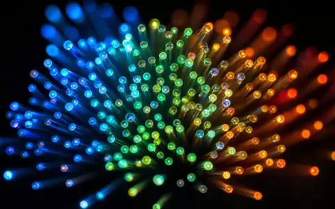 Akamai Technologies Inc. US00971T1016 macro fiber optic cable ends glowing spectrum colors dark background - Foto: THN