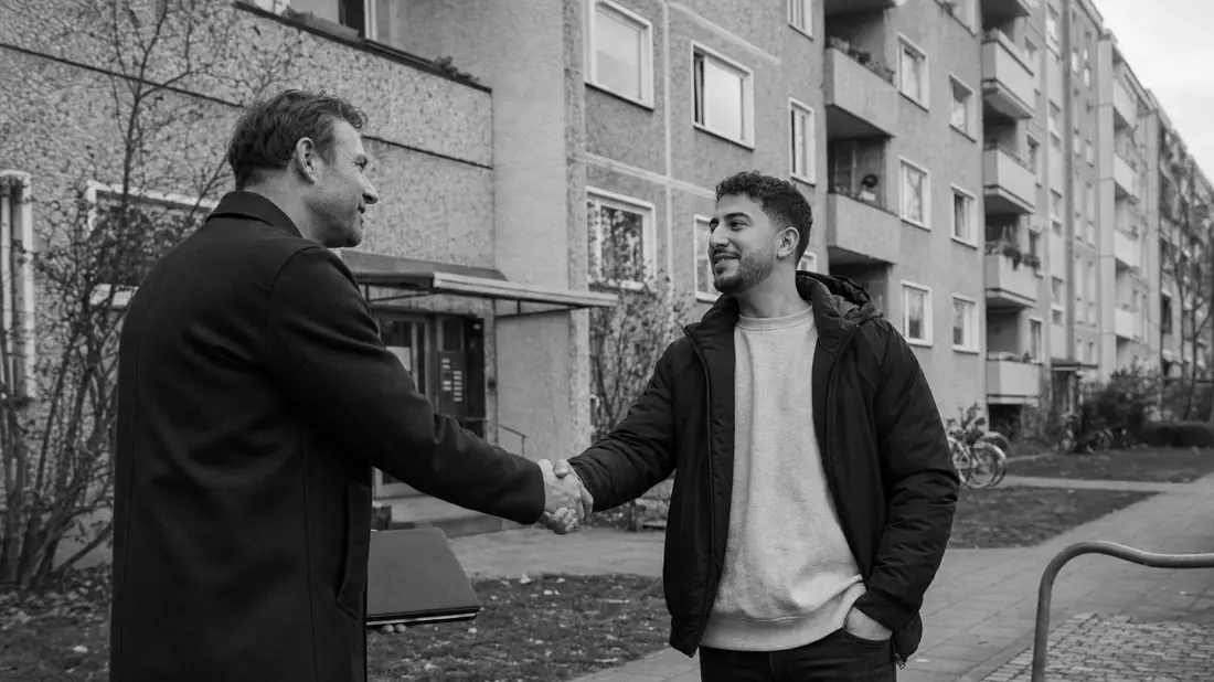Schwarzweiß-Reportagefoto: Handschlag zwischen Verwalter und Mieter vor Wohnblock