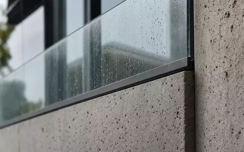 TAG Immobilien AG (DE0008303504) zeigt Materialdetail: Makroaufnahme von Fassadenbeton und Glasgeländer mit feinen Regentropfen - Foto: THN