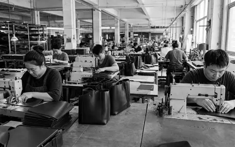 Schwarzweiße Reportagefotografie dokumentiert Fabrikarbeiter beim Nähen von Ledertaschen für Tapestry Inc. US8760301072 Investment - Foto: THN