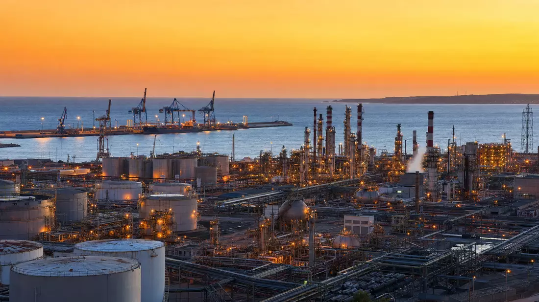 Raffinerieanlage mit Tanks und Kränen am Atlantik bei Sonnenuntergang in Portugal