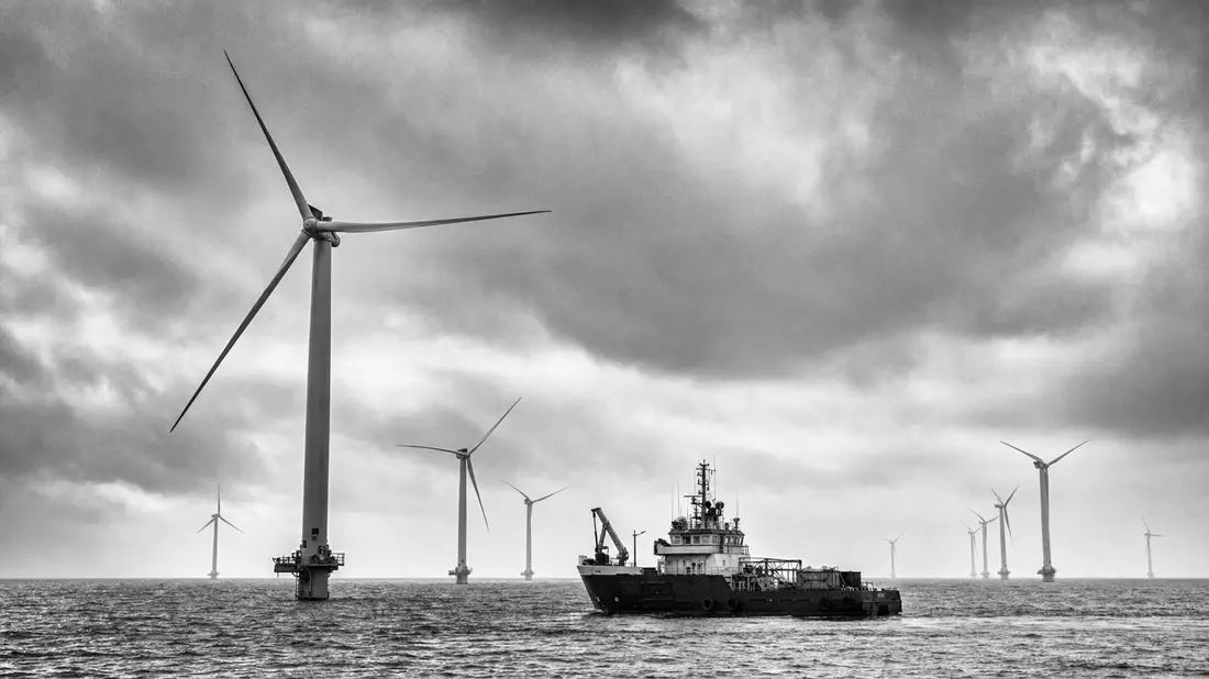 Schwarzweißfoto von Offshore-Windturbinen und Wartungsschiff auf dem Meer