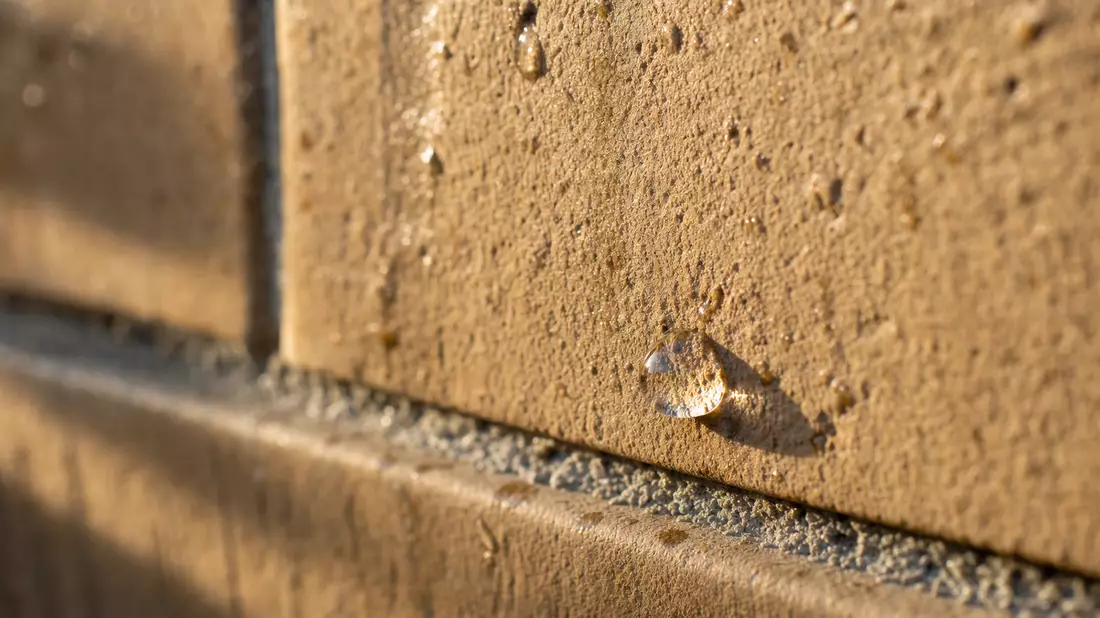 Makroaufnahme einer texturierten Ziegelfassade mit Wassertropfen im Sonnenlicht